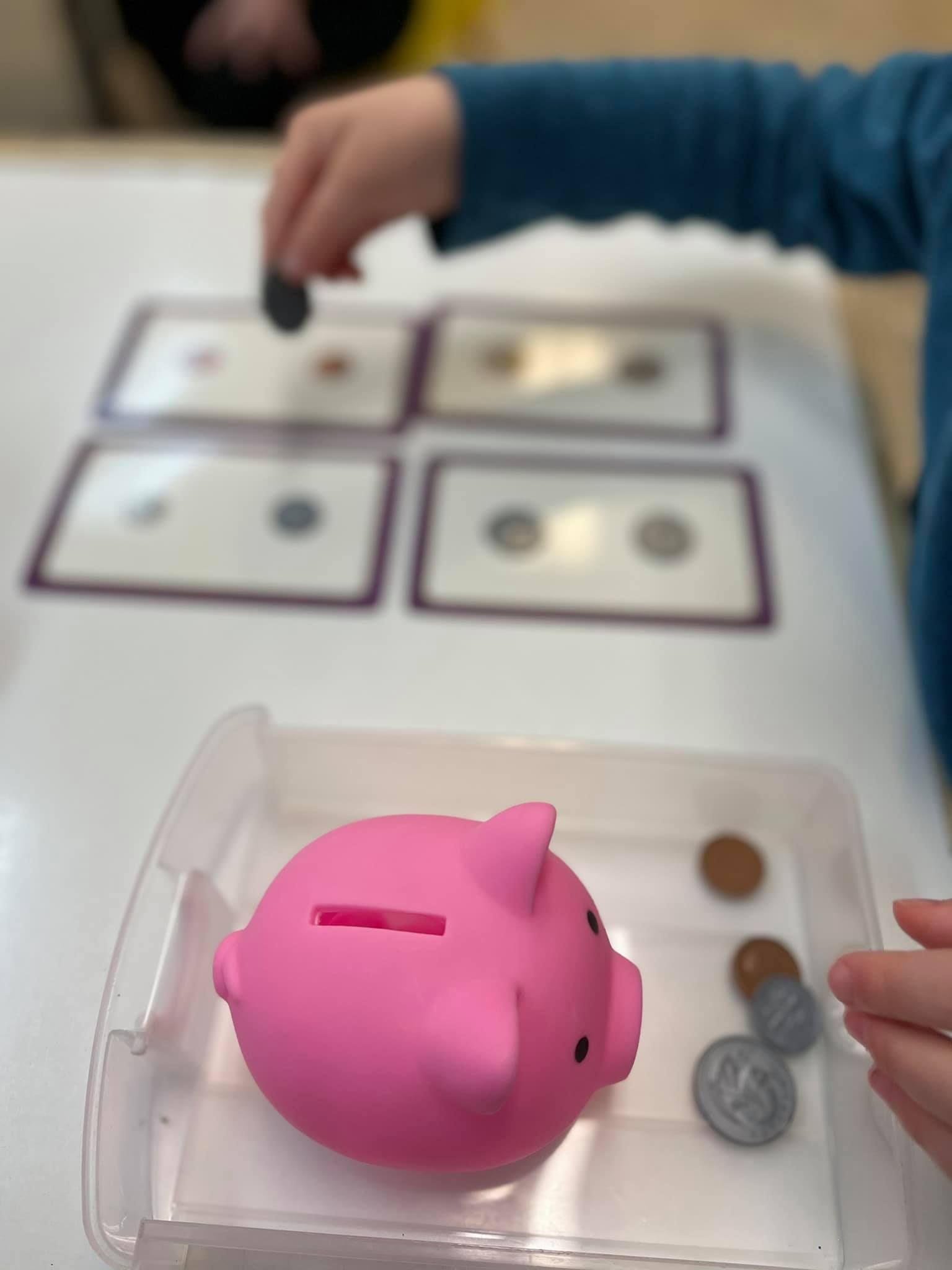Child placing a coin into a pink piggy bank