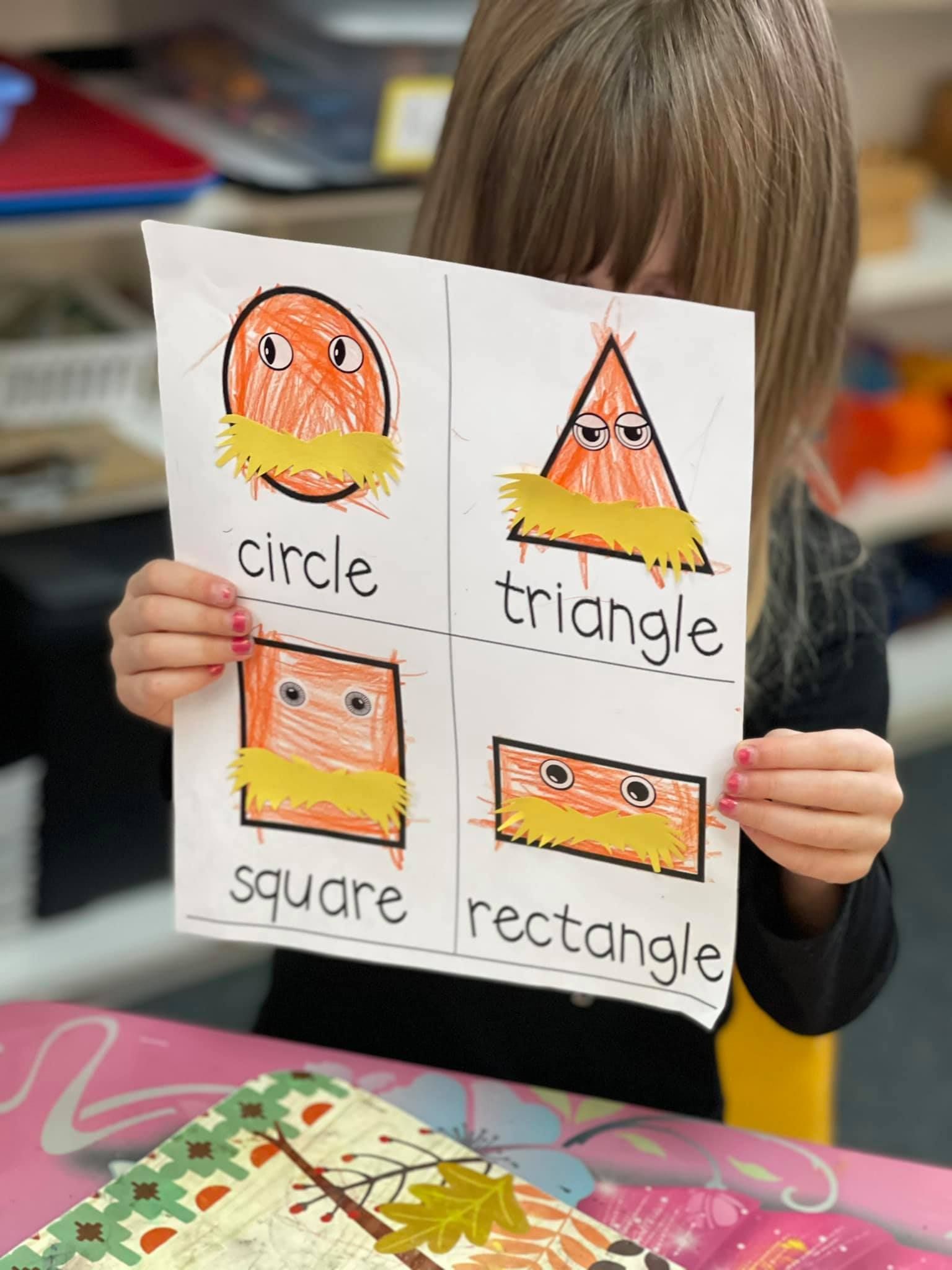 Young child holding a paper with drawn shapes and label