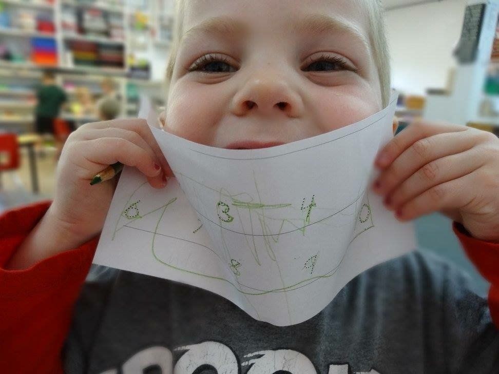 Smiling child holding a paper with green numbers drawn on it