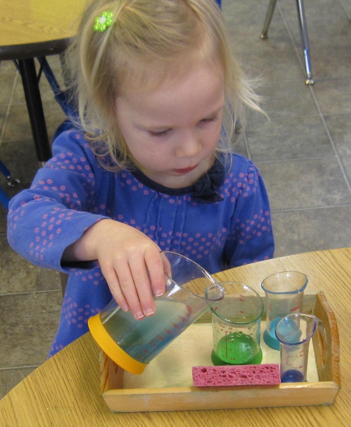 Young girl pouring colored liquid from a pitcher into a glass on a tray