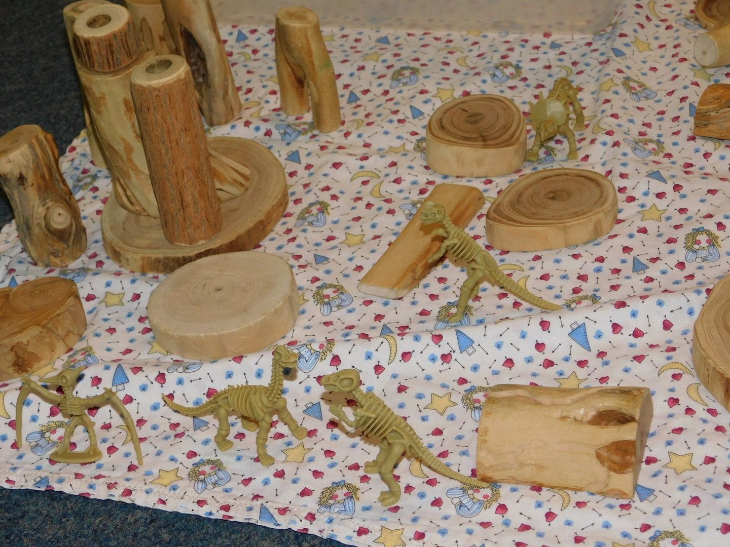 Toy dinosaurs among wooden blocks and stumps on a patterned surface
