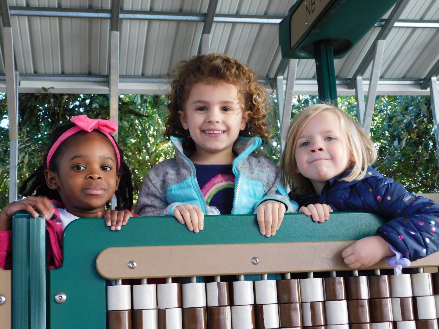Three smiling children playing a musical instrument on a playground