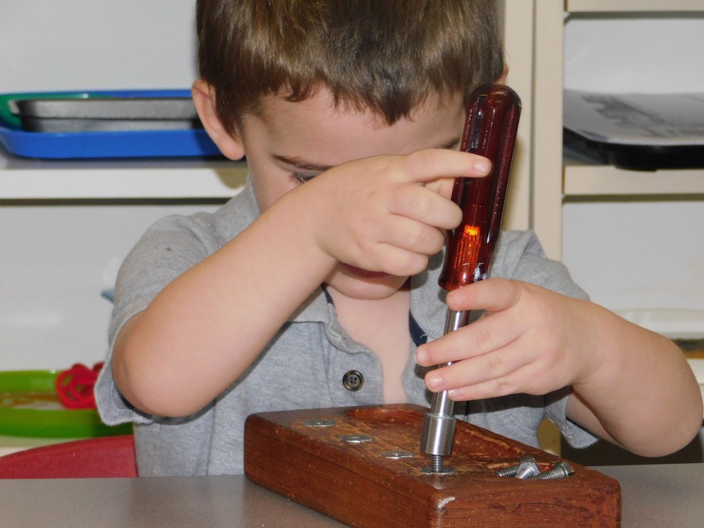 Boy using a screwdriver to screw into a wooden block