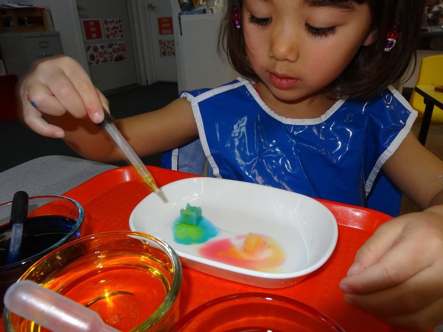 Young girl using a dropper to add colorful liquid to a dish.