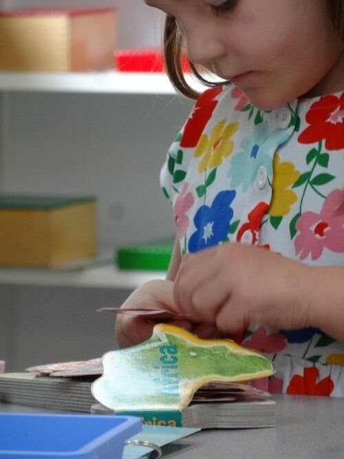 Girl in floral top focuses on continent puzzle, hands at work