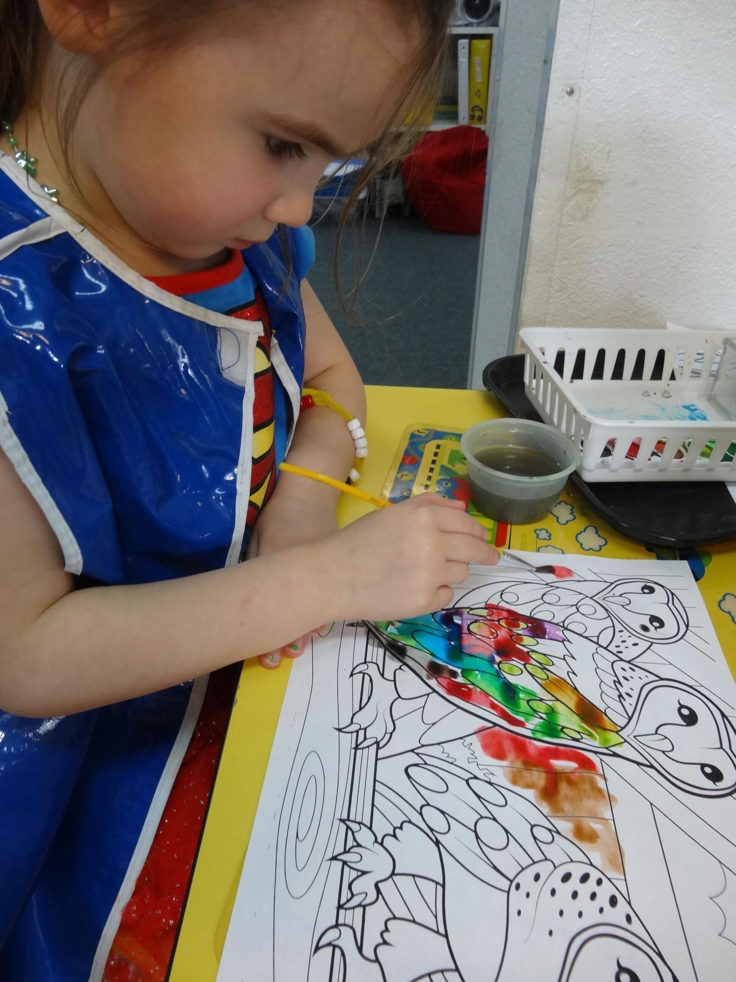 Girl painting with watercolors at a table, wearing a blue smock