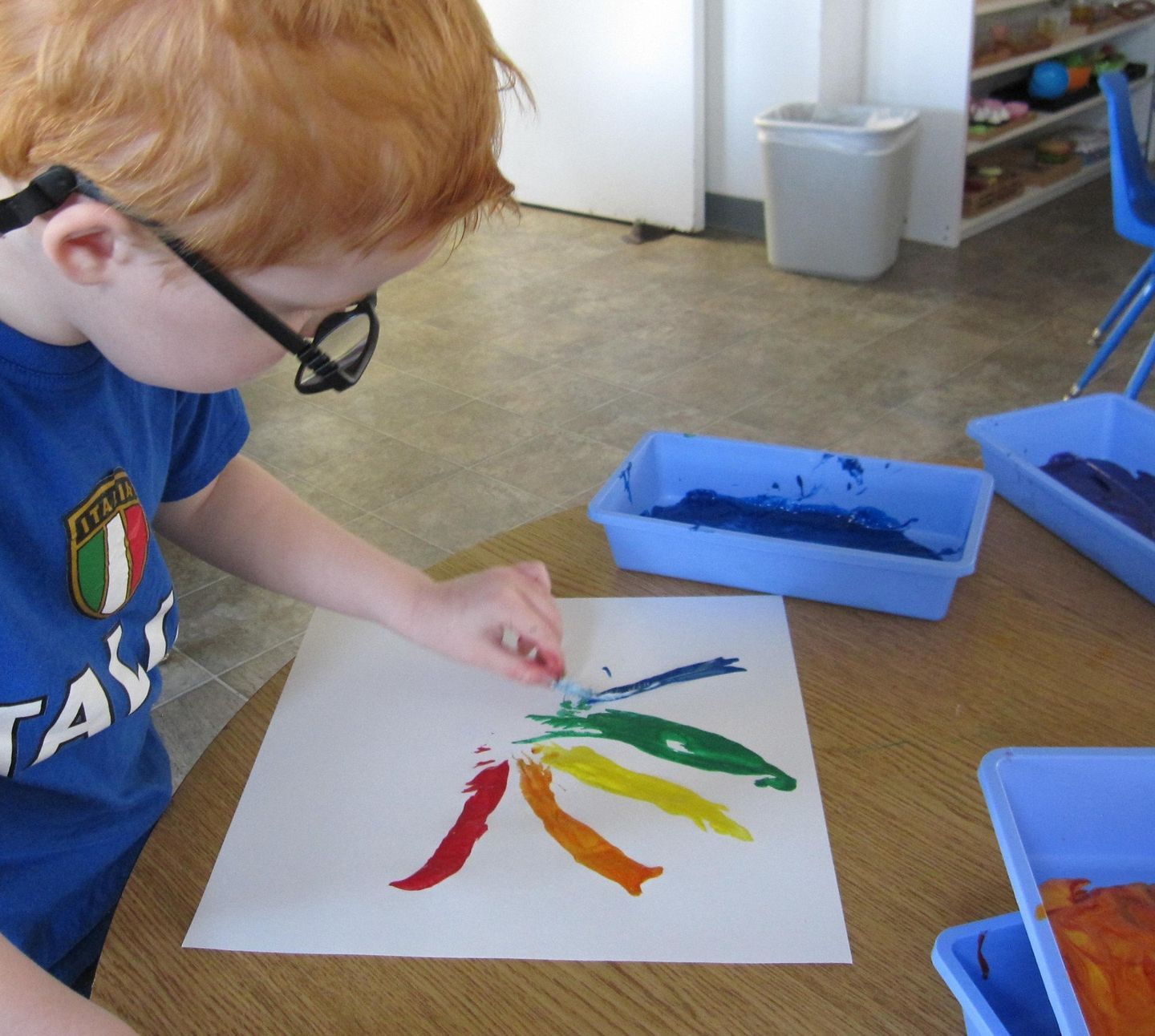 Young child with glasses painting a rainbow with finger paint
