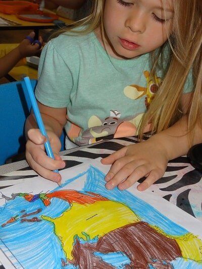 Girl with blonde hair coloring a drawing with a blue pen