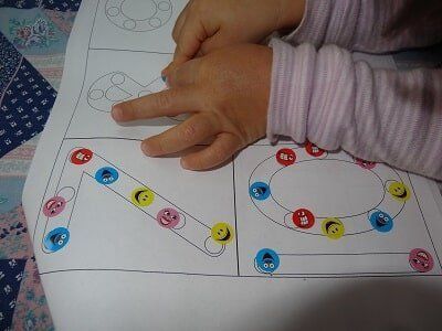 Child's hands tracing shapes on a worksheet with colorful smiley-face marker