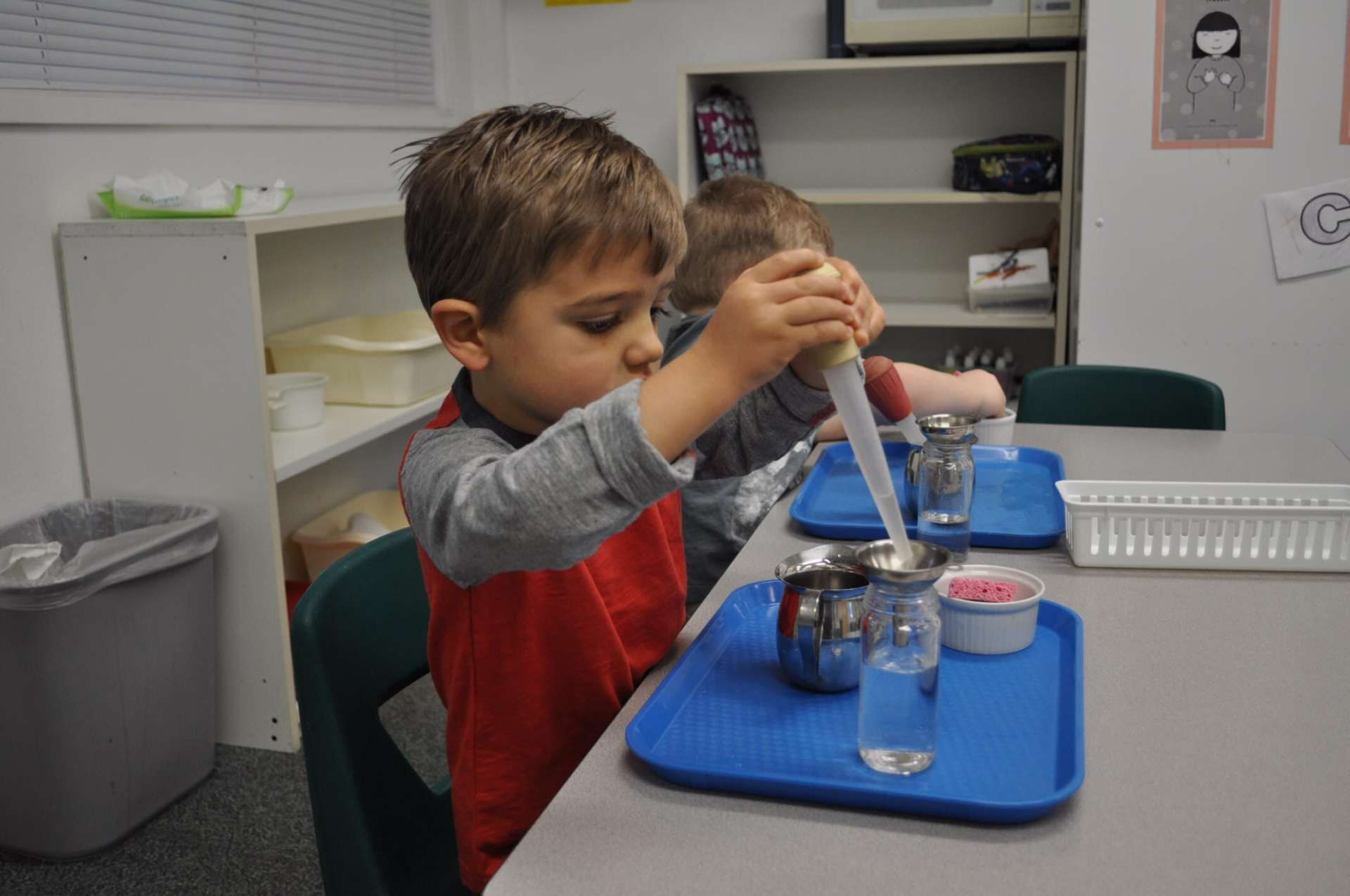 Boy using a dropper to transfer liquid from a bottle into a small metal container at a table