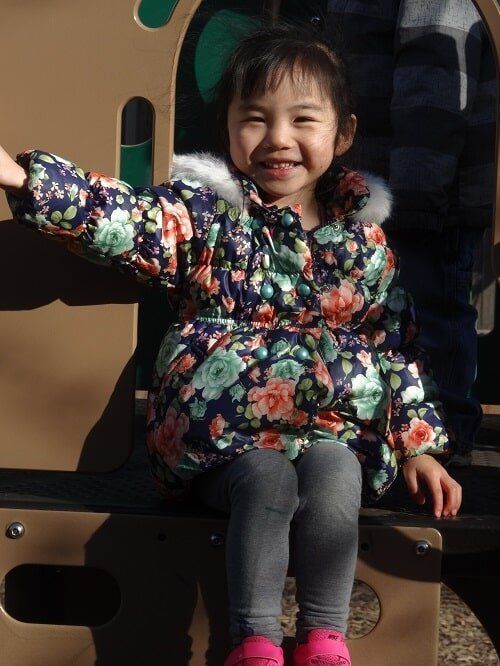 Young girl in floral coat smiles, sitting outside
