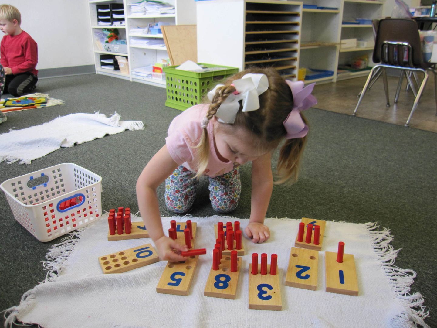 Girl arranging red sticks on number tiles in a classroom setting