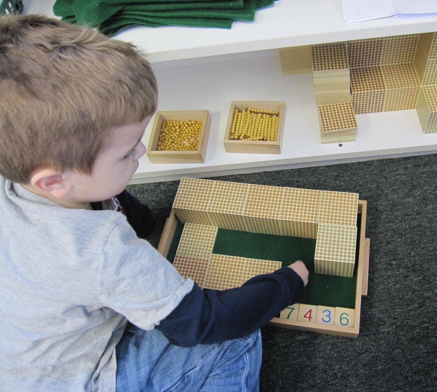 Young child using Montessori math materials, wooden blocks, cubes, rods and trays