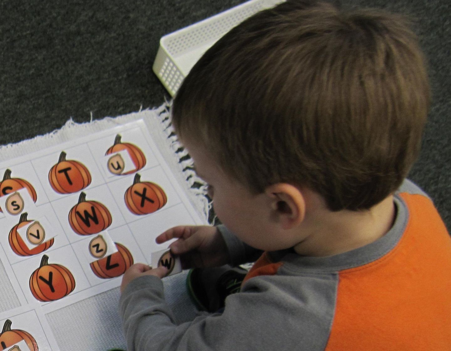 A young child matching uppercase letters to pumpkin-shaped cutouts