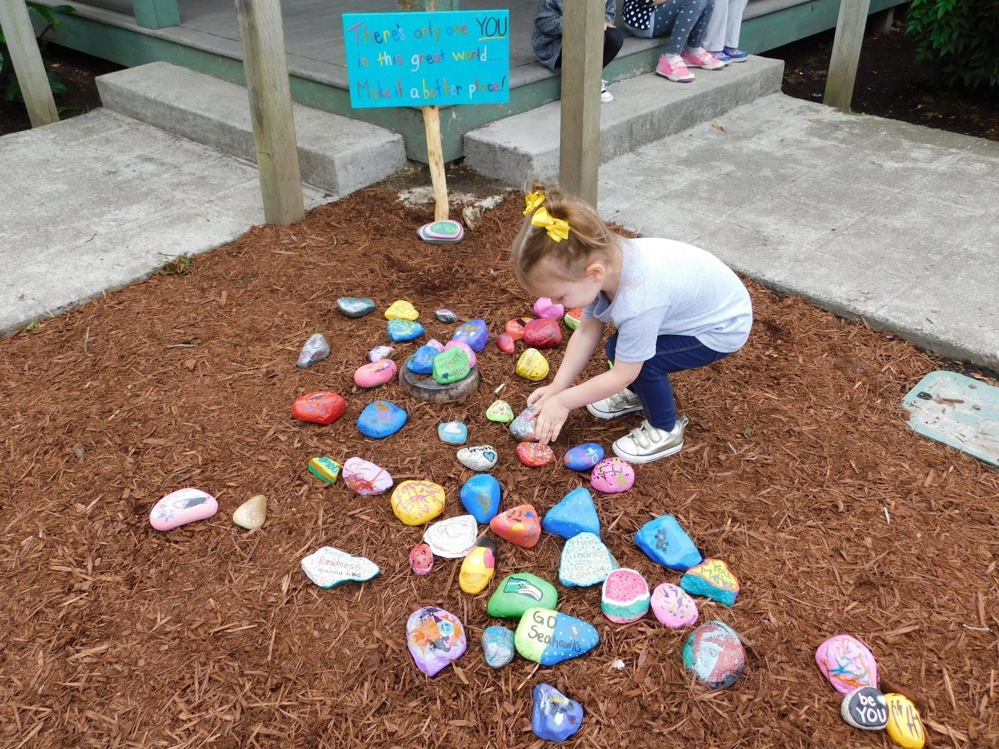 Girl in blue jeans and t-shirt playing with painted rocks in a mulched area