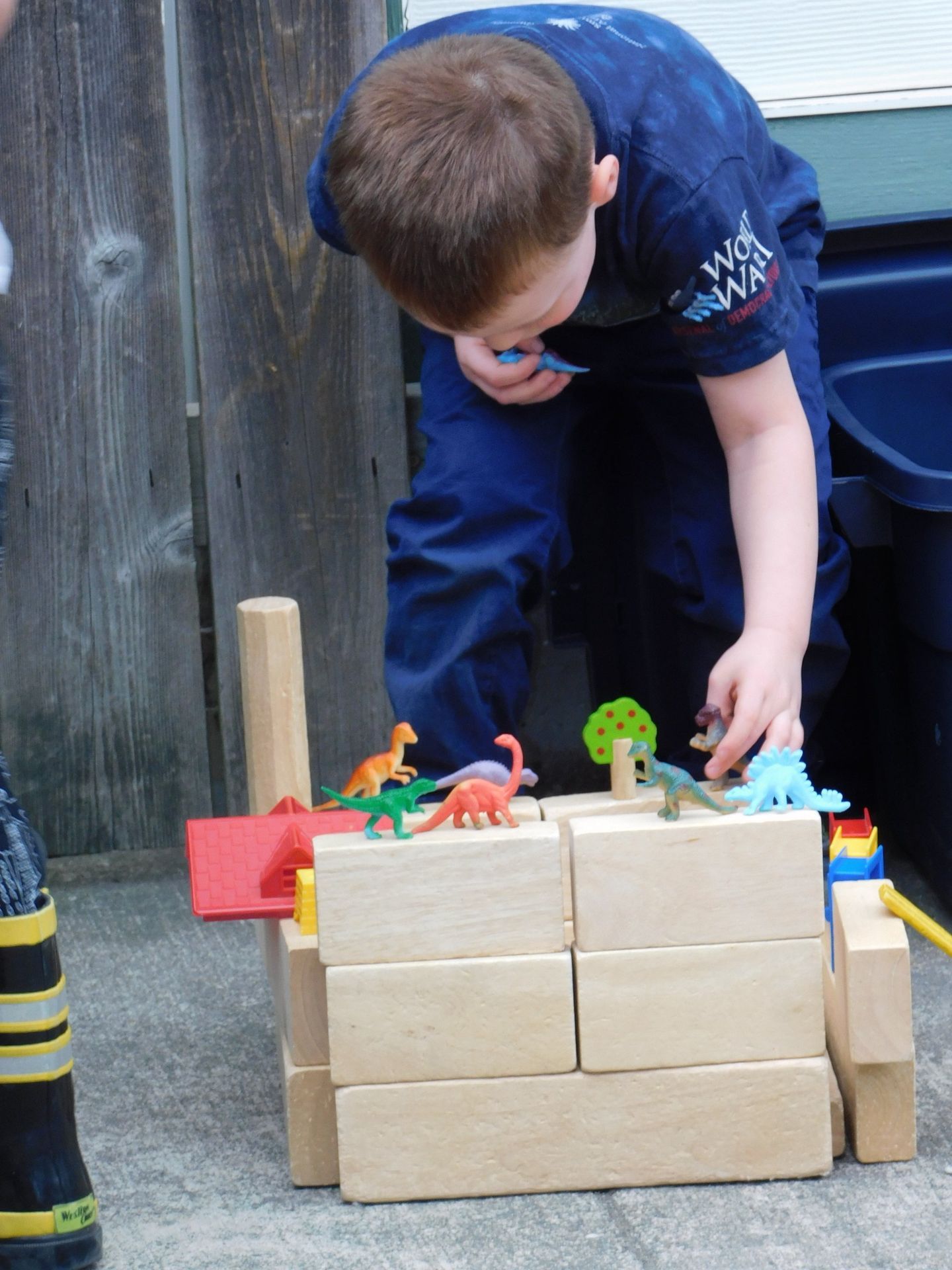 Boy building a structure with wooden blocks, adding toy dinosaurs