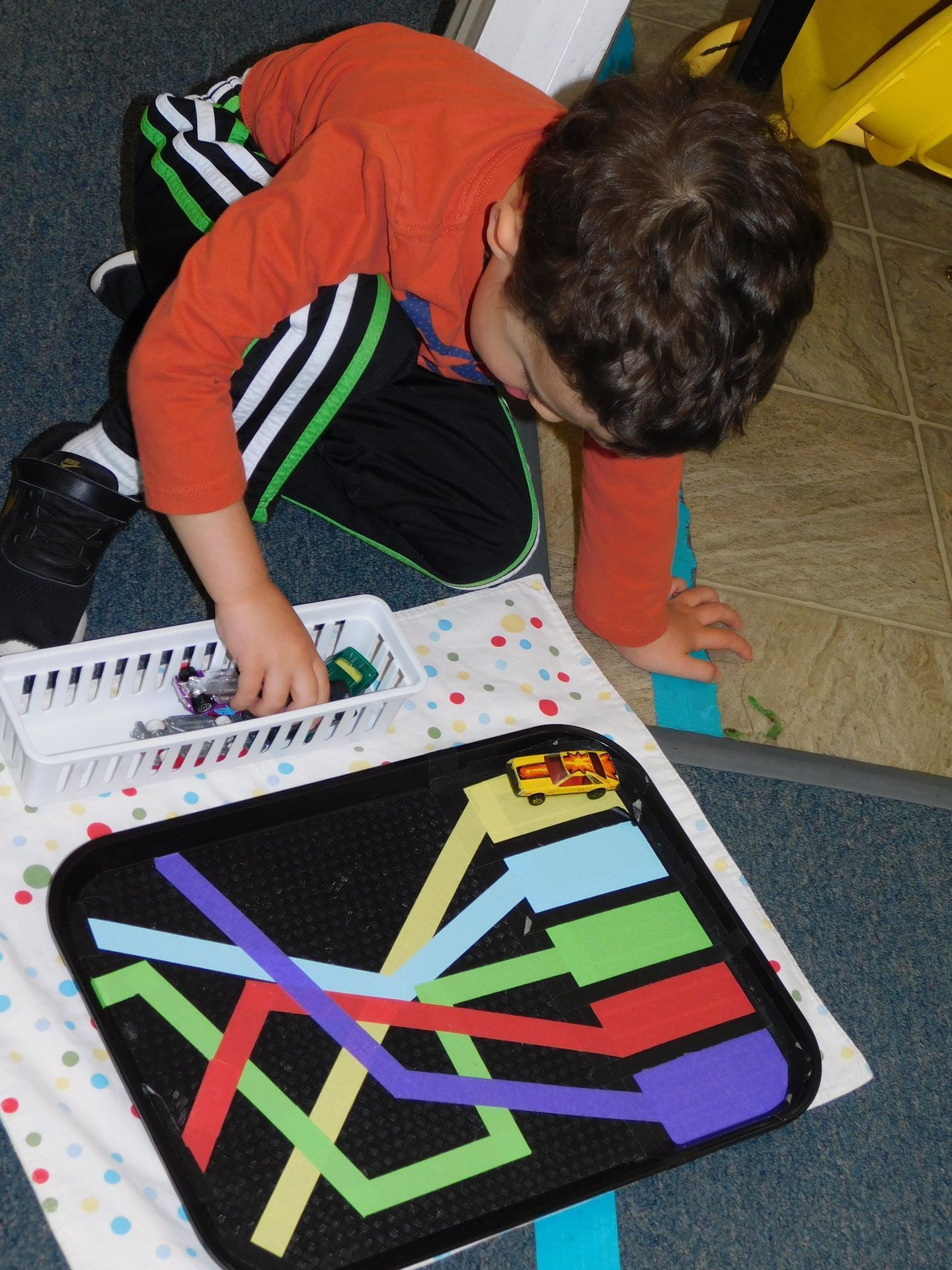 Boy playing with toy cars on a colorful track mat in a room