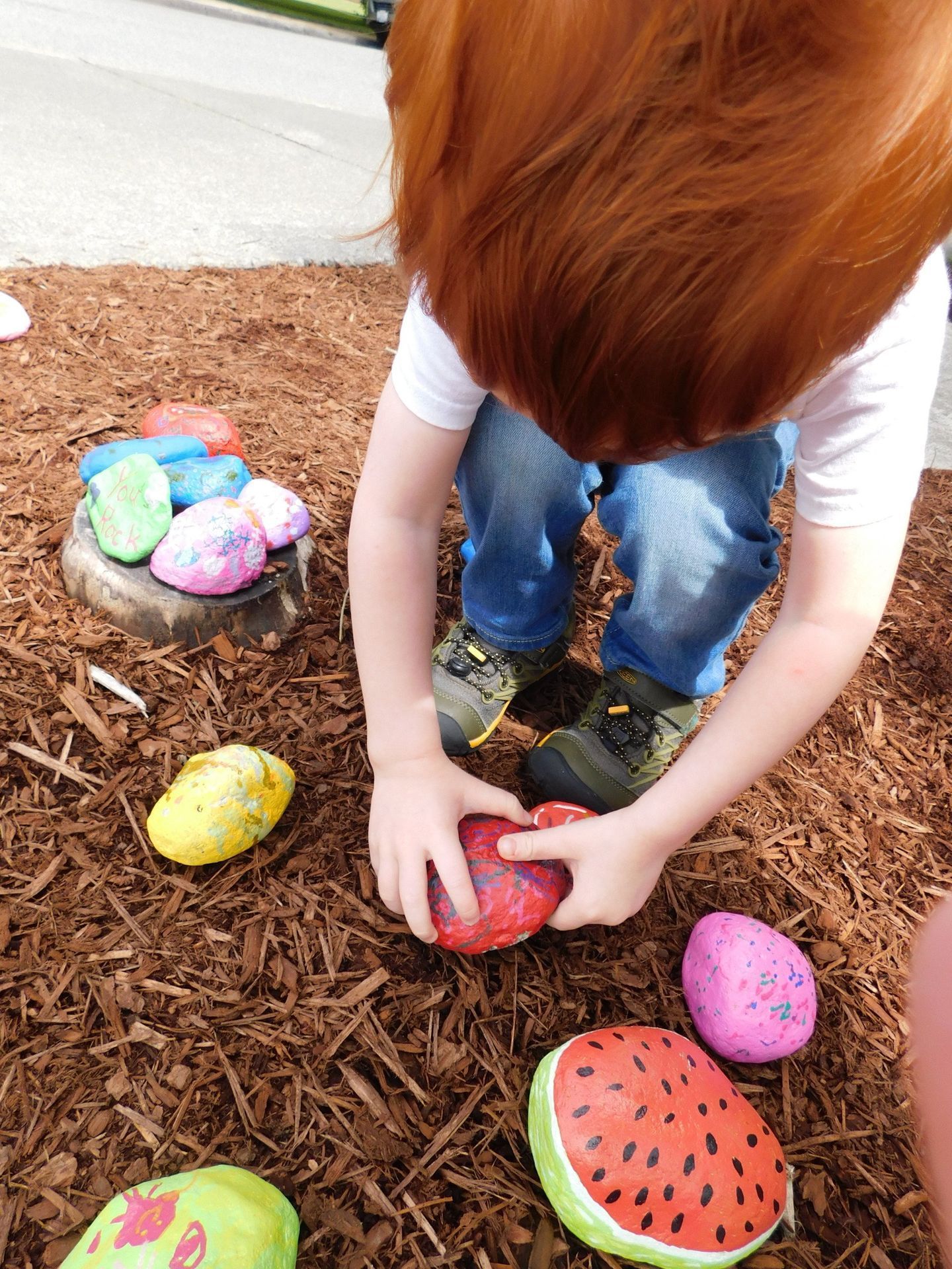 Child with red hair playing with painted rocks in wood chips