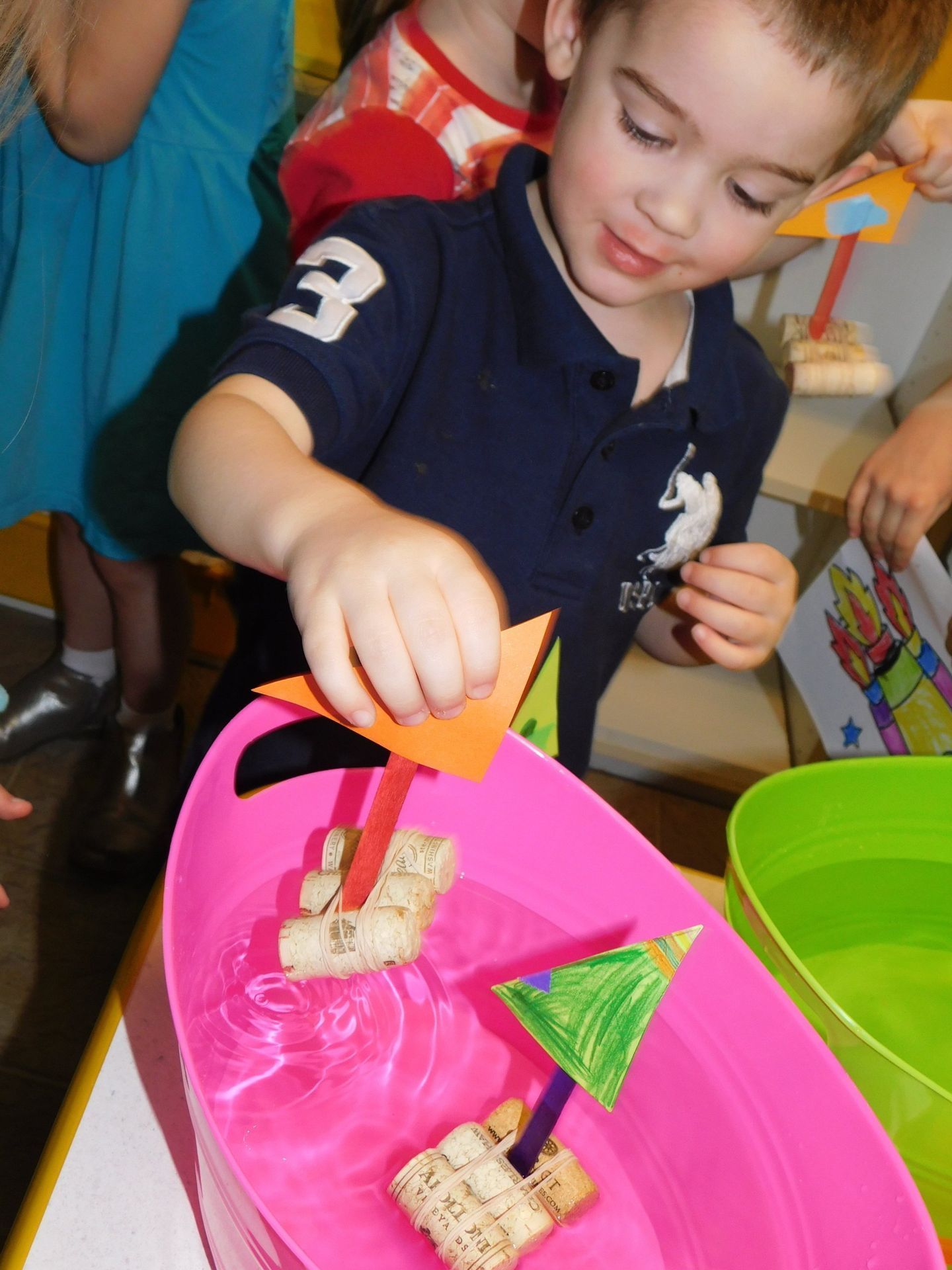 Young boy plays with toy boats in a pink tub of water, craft activity