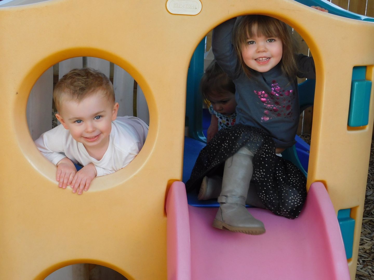 Children playing in a yellow and blue playhouse with a pink slide