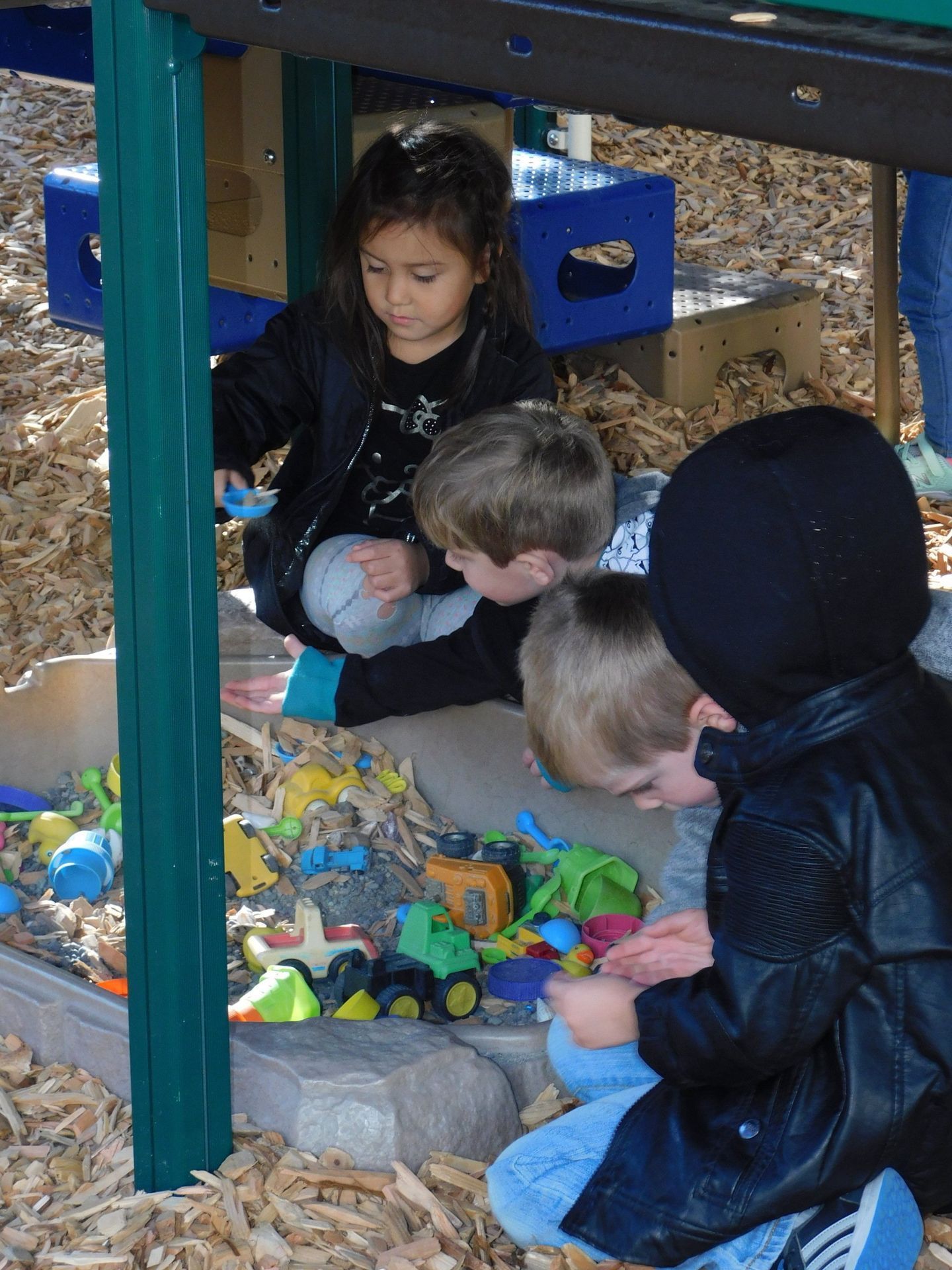 Children playing with toy trucks in a sandbox, one girl, three boys