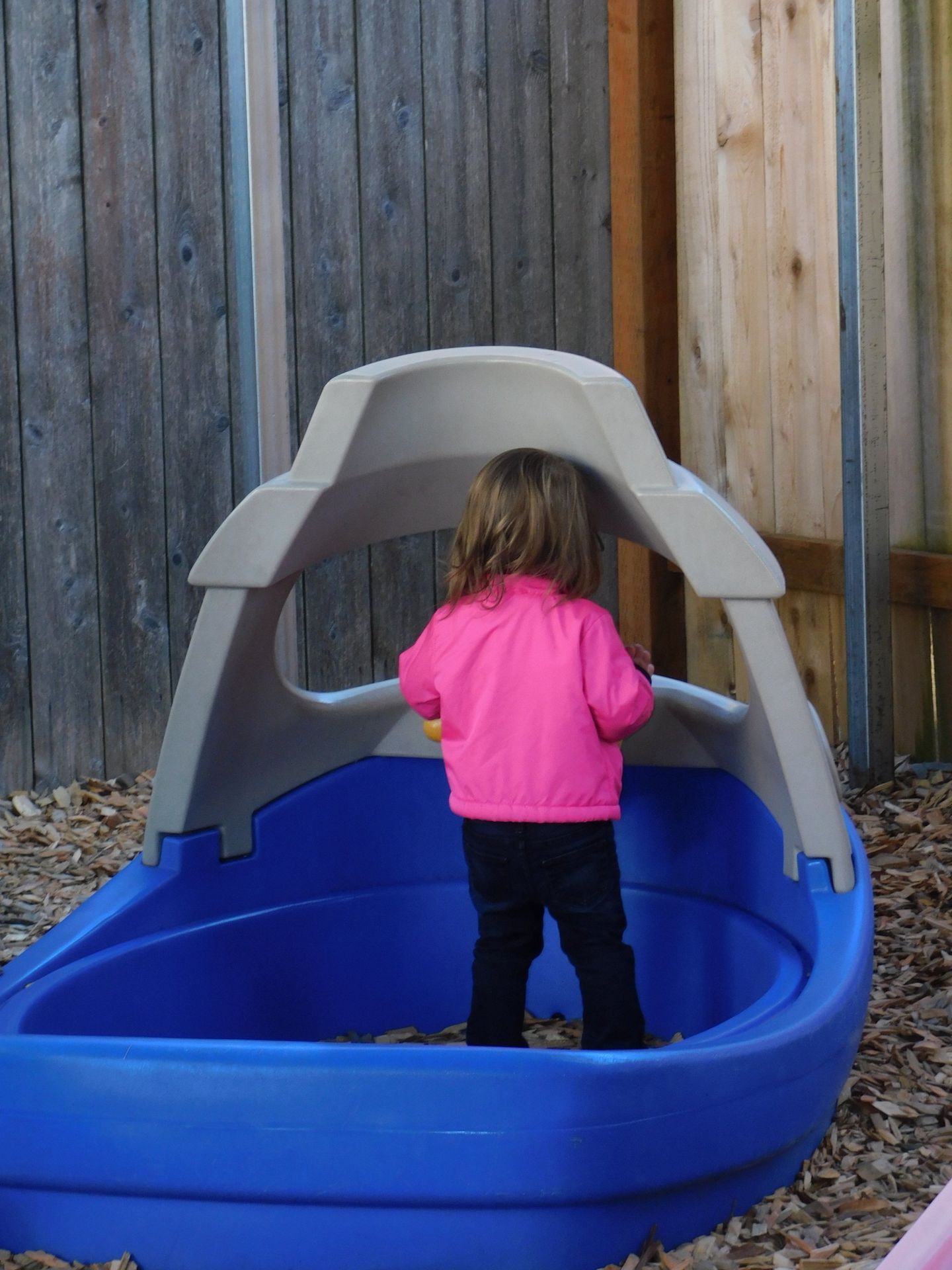 Girl in pink jacket plays in blue sandbox
