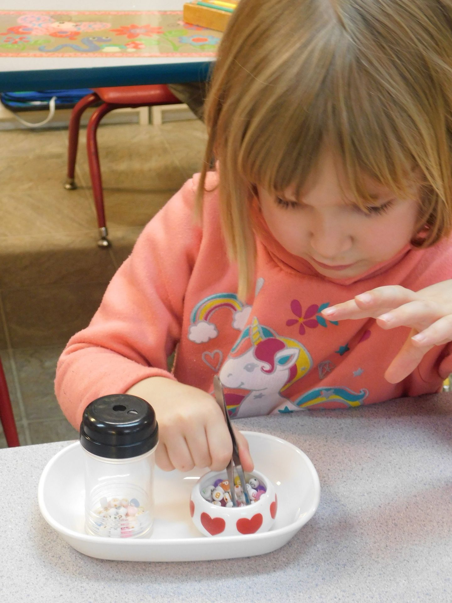 A young girl concentrates on arranging small crayons in a tray at a table indoors