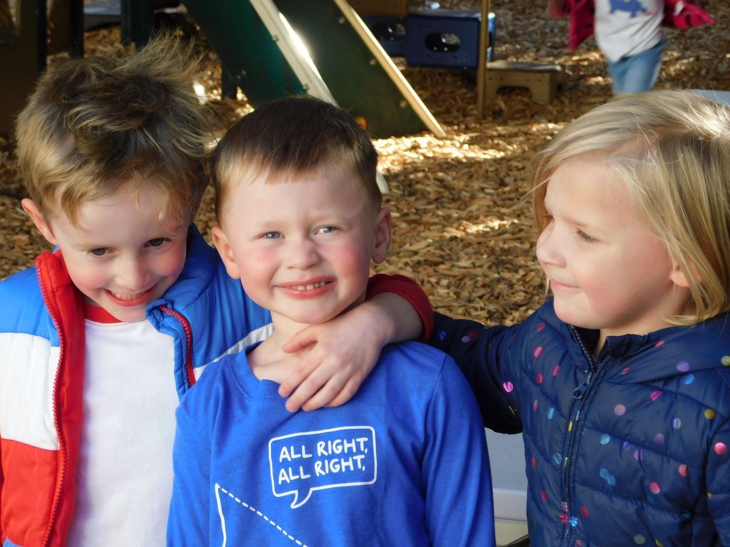 Three young children smiling together outside