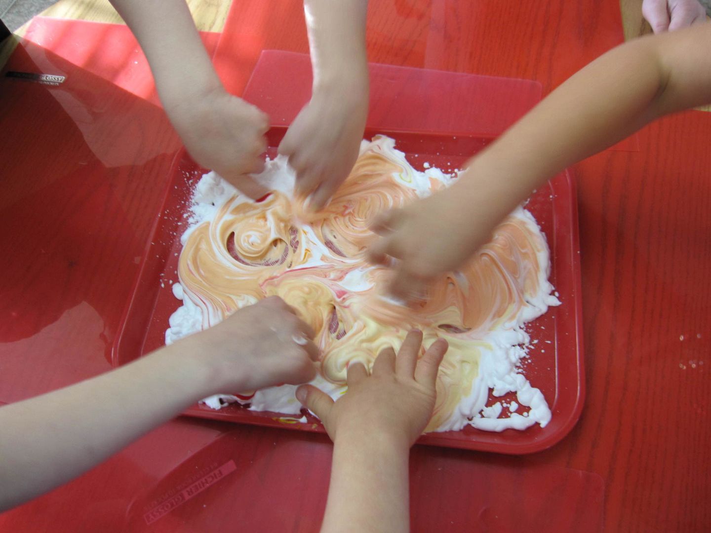 Hands mixing orange and white paint in a red tray on a red table
