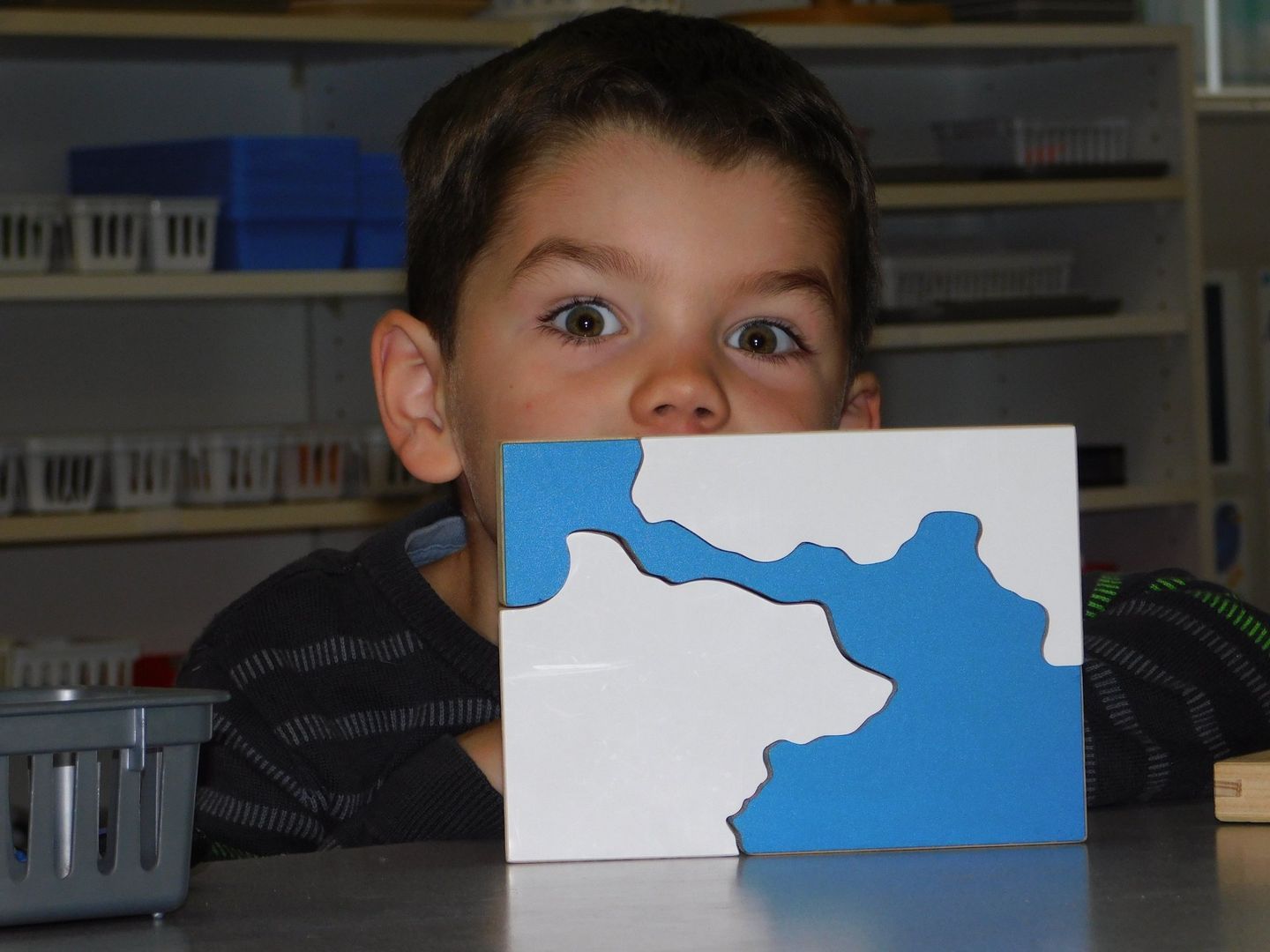 Boy with wide eyes peers at a puzzle showing a blue and white landmass