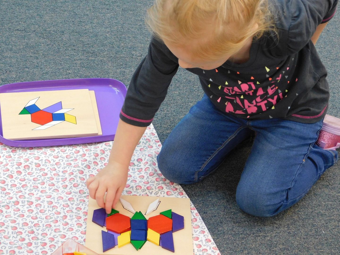 Girl on floor assembling a butterfly puzzle with colorful geometric shapes