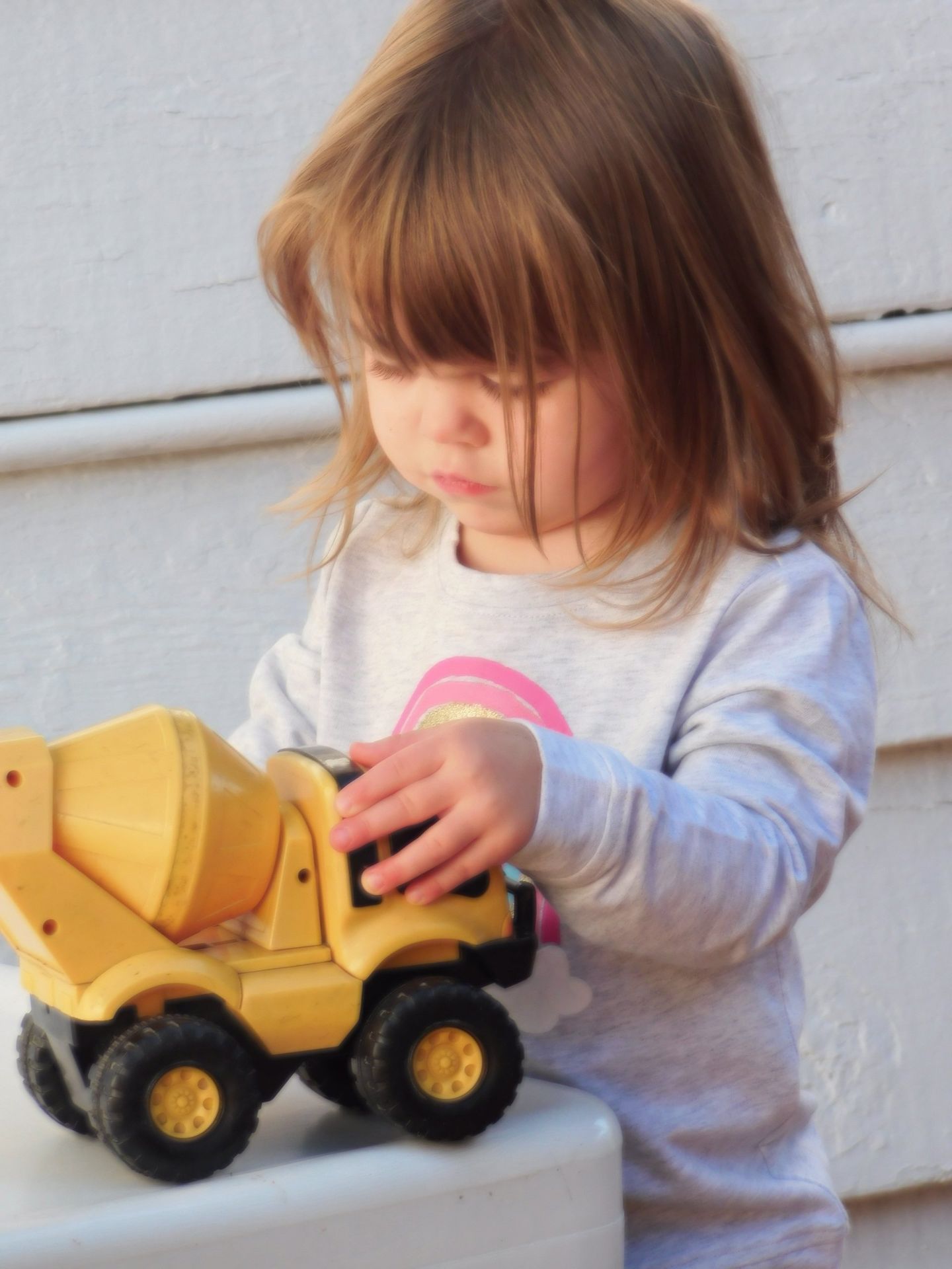 Young child with brown hair playing with a yellow toy cement truck on a white step