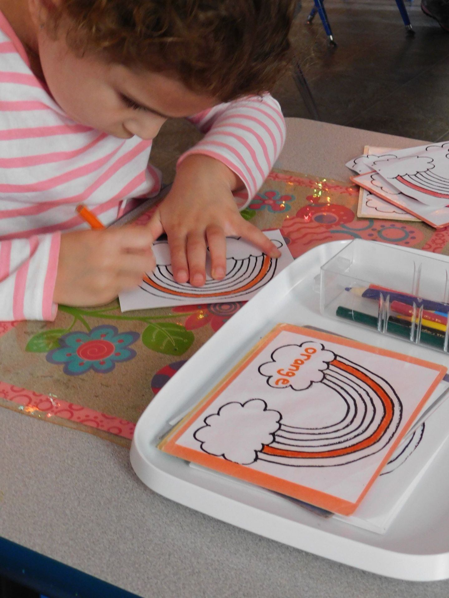 Young child coloring a rainbow on a card at a table