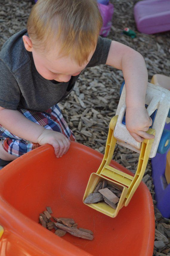 Young child playing with toy truck, filling orange bin with wood pieces