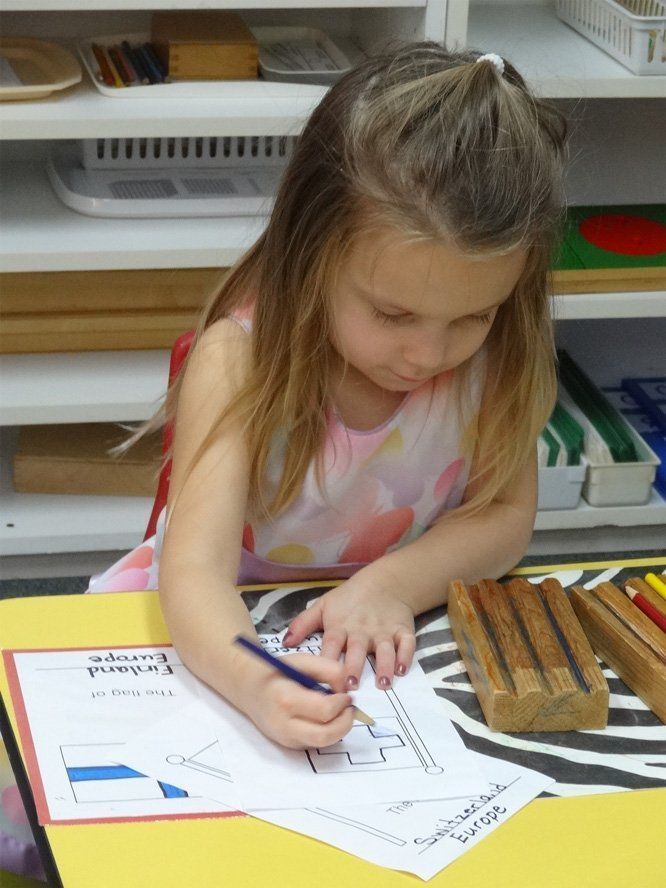 Young girl coloring a map of Europe with colored pencils at a desk in a classroom