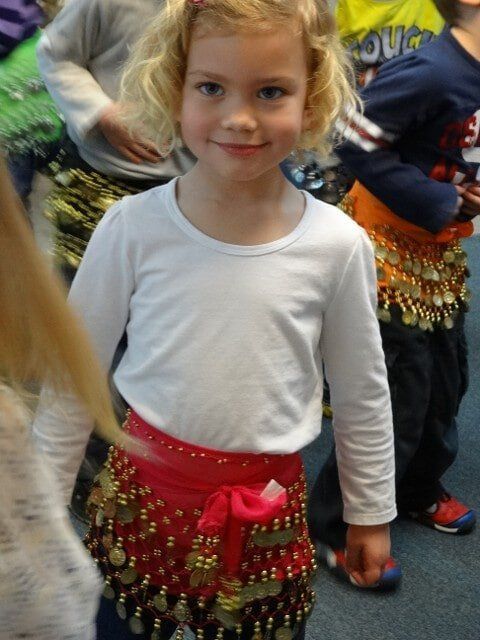 Blonde girl wearing white shirt and red belly dance skirt with coins, smiling