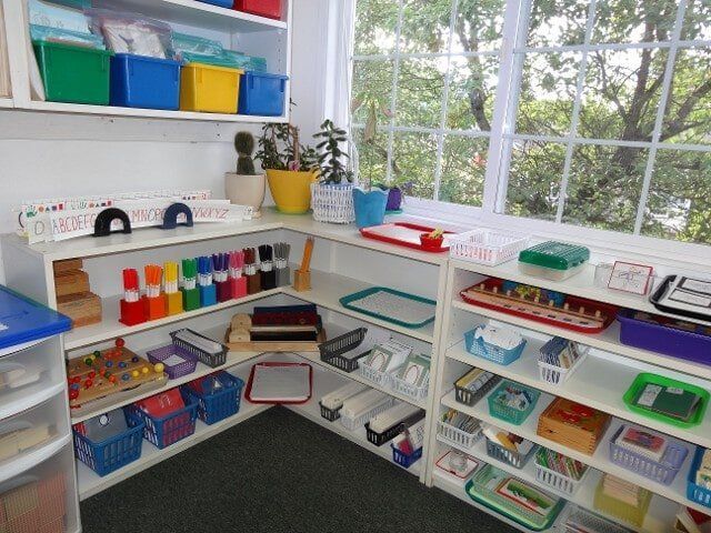 A Montessori classroom corner, with shelves of learning materials in a bright, organized space by a window