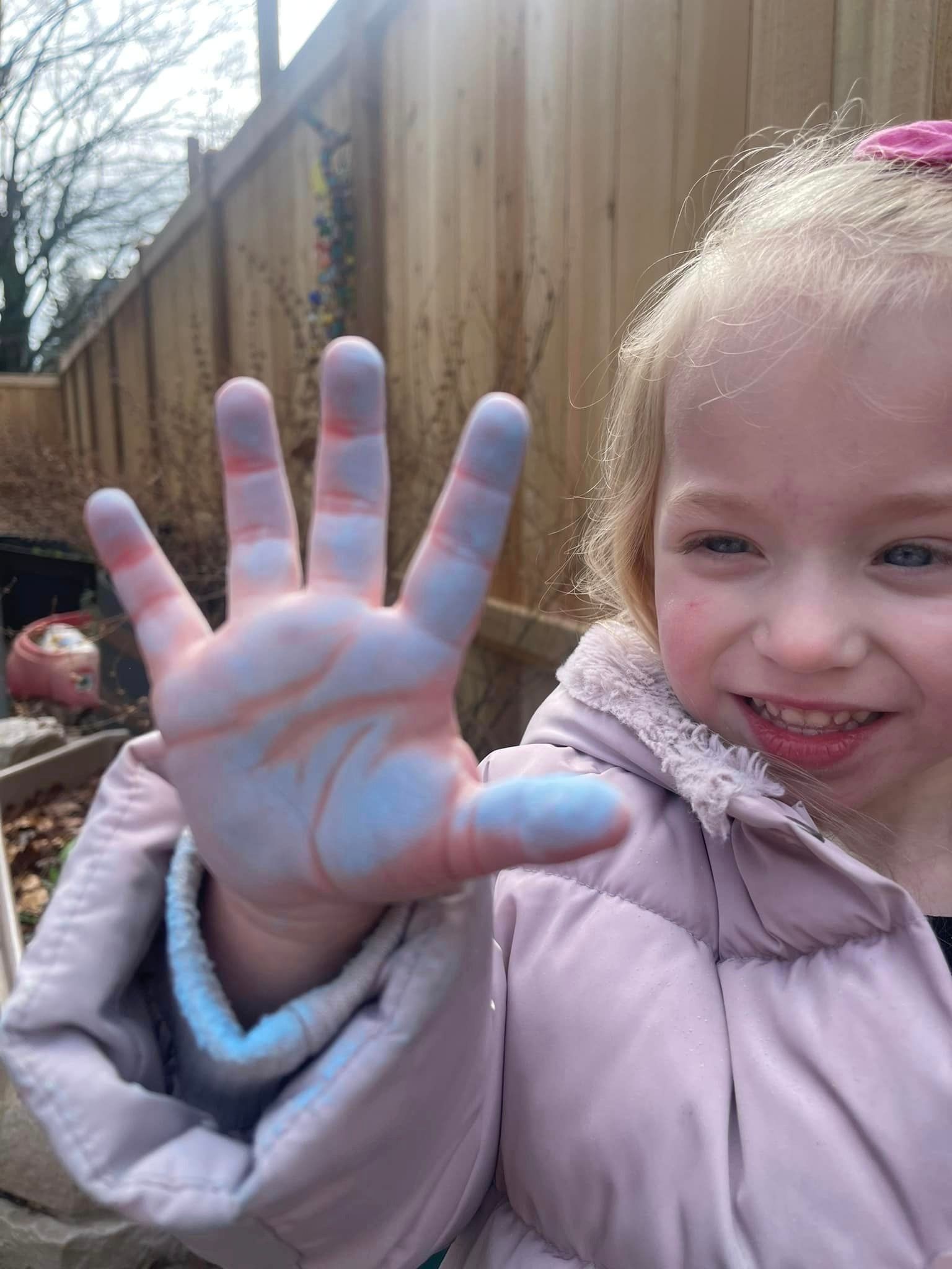 Girl with blue and pink paint on her hand, smiling outdoors