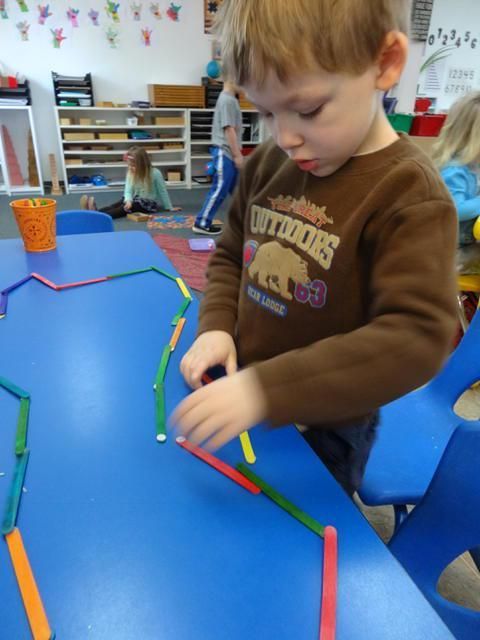 Boy arranging colorful popsicle sticks on a blue table in a classroom