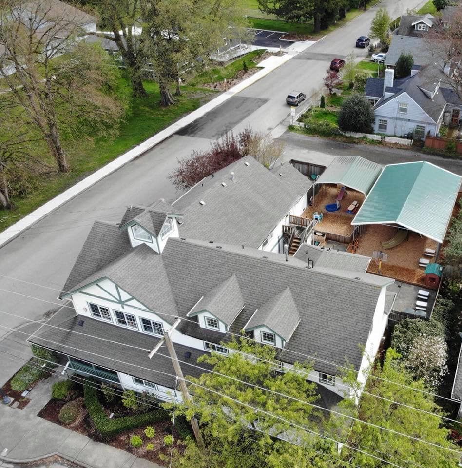 Aerial view of a white building with dark grey roof, next to a street with cars