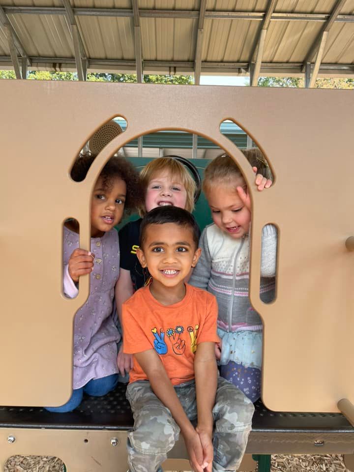 Four young children peeking through a playground opening, smiling