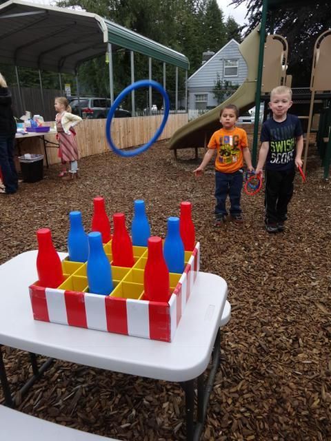 Two boys at an outdoor game with red and blue bottles, a hoop, and a striped table