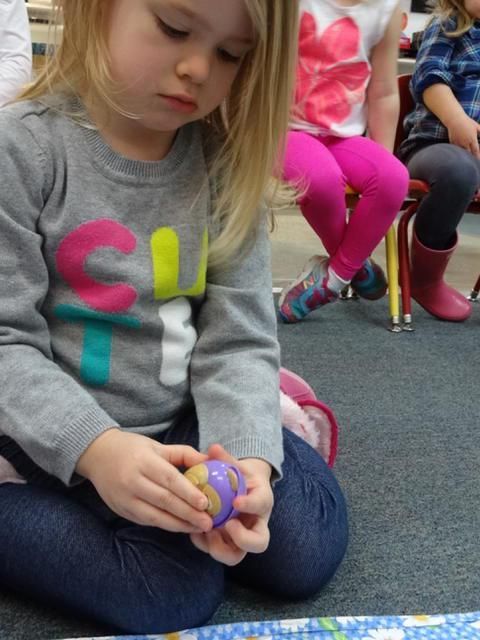 A young girl with blonde hair sits cross-legged, playing with a toy