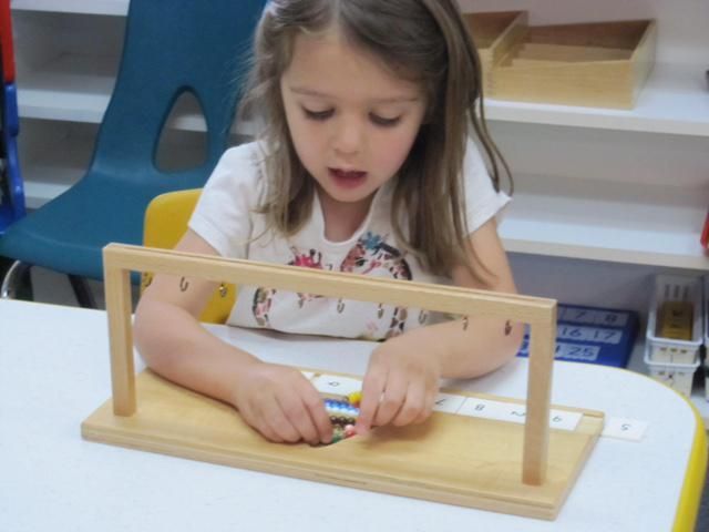 Girl using a wooden math counting frame with colored beads at a table,