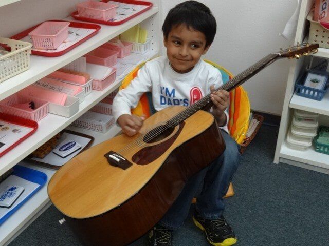 Boy in a white shirt plays an acoustic guitar