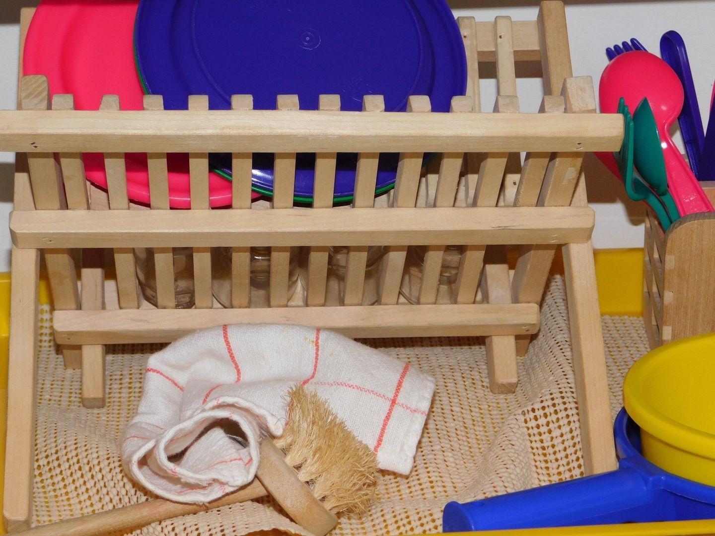 Wooden toy dish rack with colorful plates, utensils, a cloth, and a brush