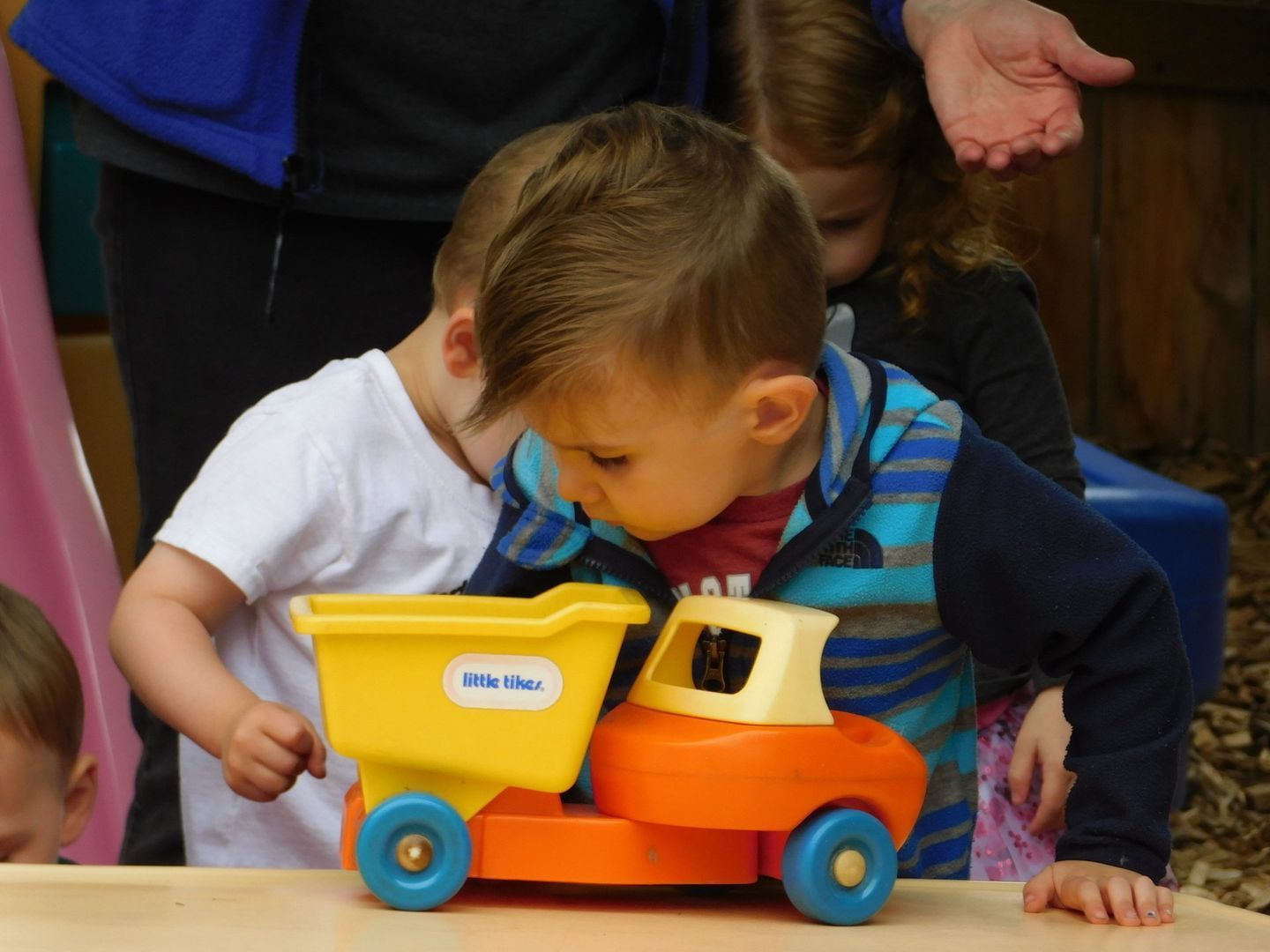 Two toddlers examining a bright yellow and orange toy truck, outdoors