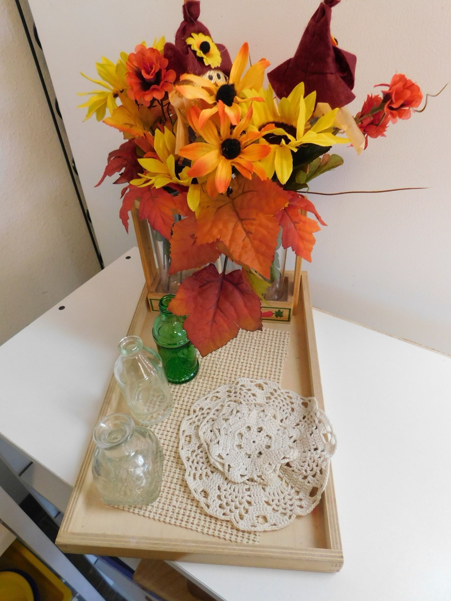 Fall-themed display: sunflowers, red leaves, decorative bottles and doilies on a wooden tray