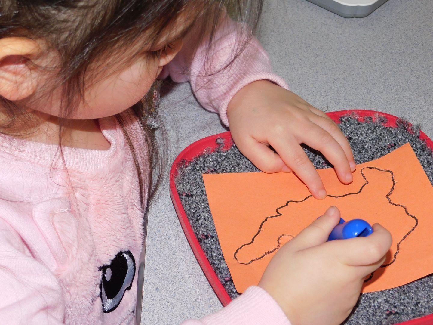 Young child, in pink, traces a black line on orange paper
