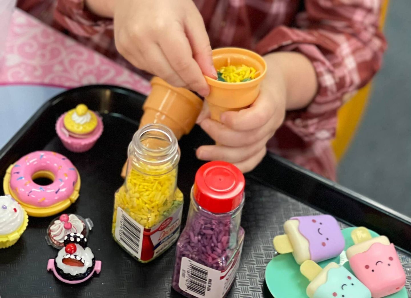 Child playing with toy food: cones, cupcakes, donuts, sprinkles.